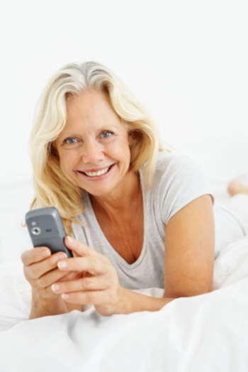 Senior woman with a mobile phone relaxing on bed